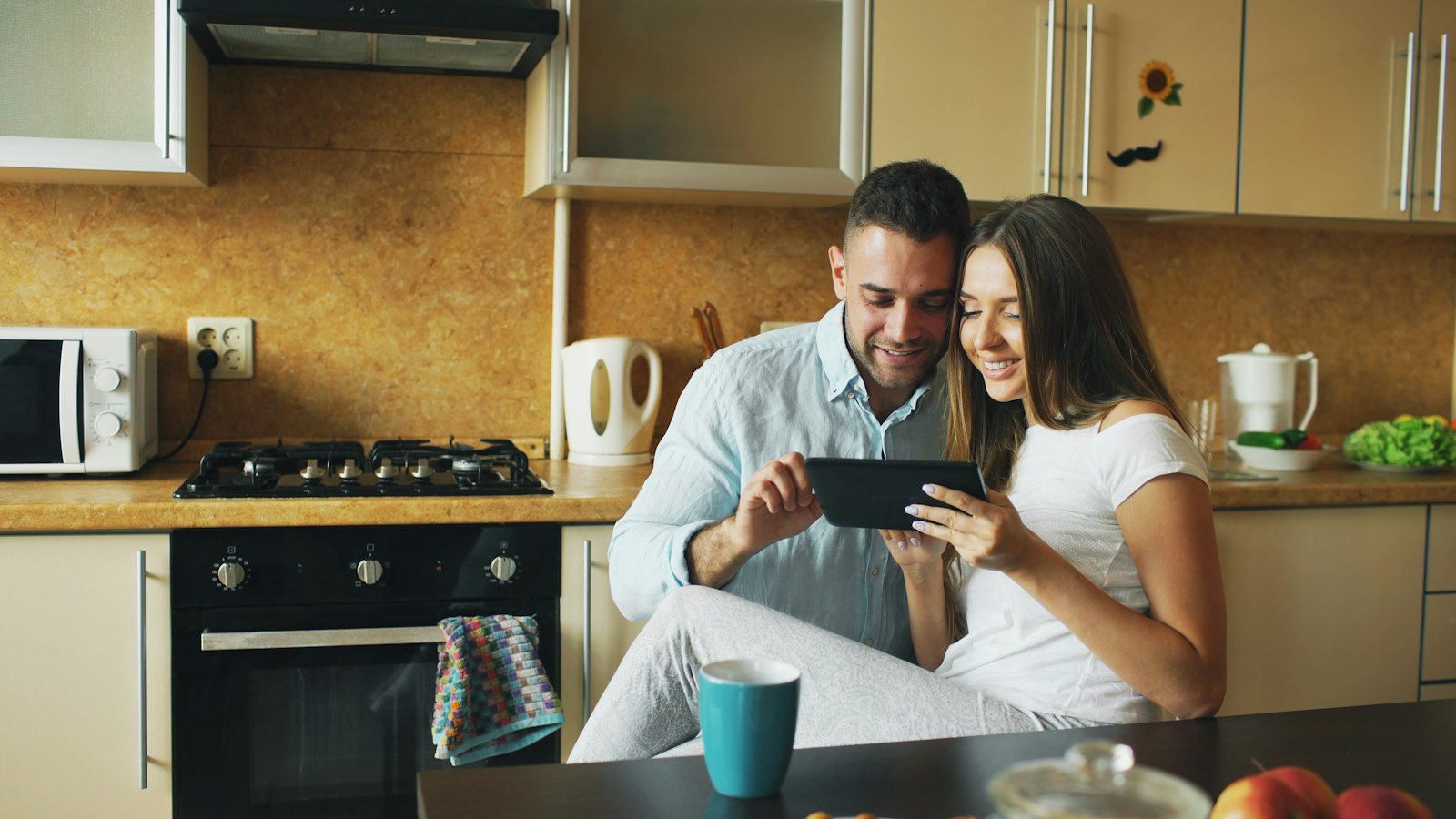 A smiling couple shopping online together on a tablet in their kitchen